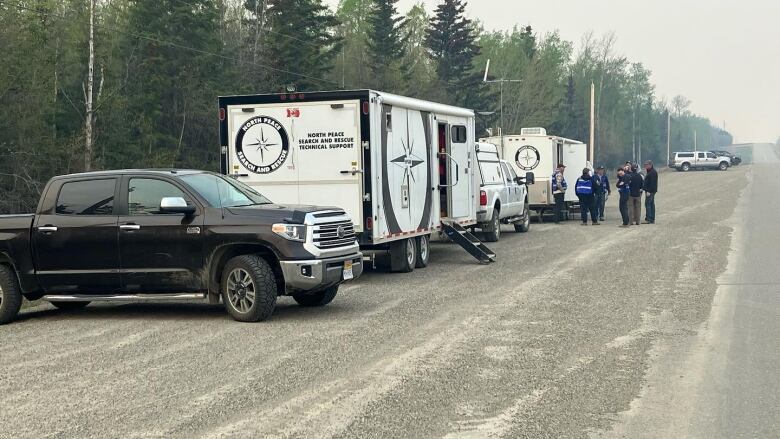 Members of the North Peace Search and Rescue team assist the RCMP delivering evacuation alerts and orders related to the Red Creek Fire. Photo shows multiple rescue vehicles lined up on a dusty dirt road.