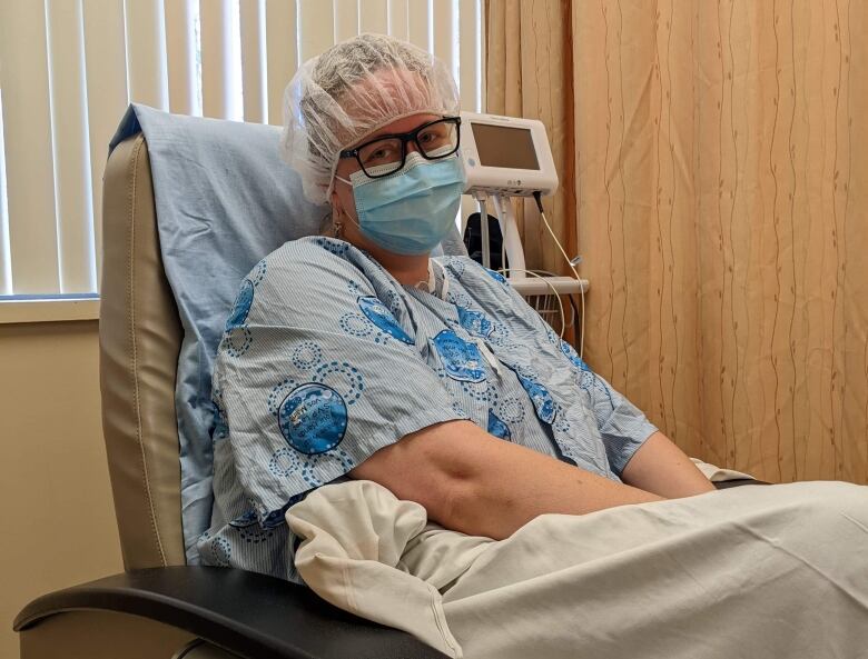 A woman in a mask and hair nets on a hospital bed.