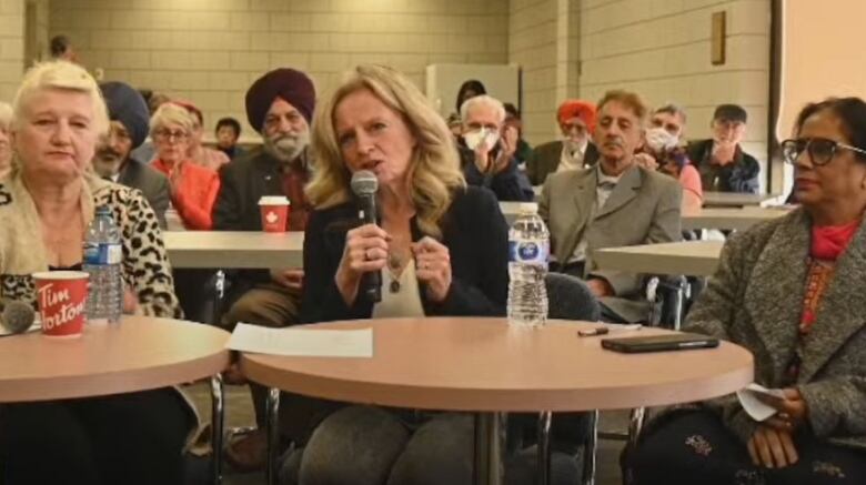 A woman sits at a table in front of many other people.