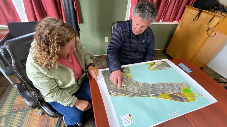 A woman and a man sit and a desk looking at a colour map of the community. 