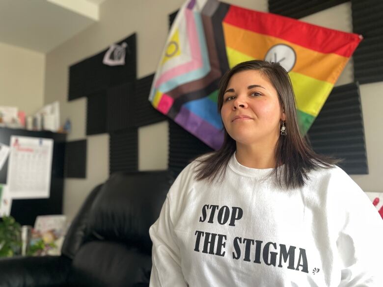 A woman standing in an office wearing a white sweater with the words Stop the Stigma on it.