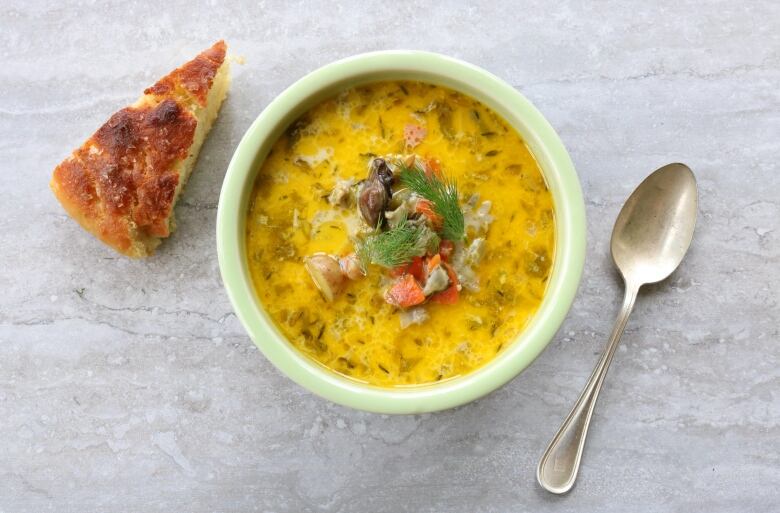 A bowl of chowder with a spoon and a piece of bread.