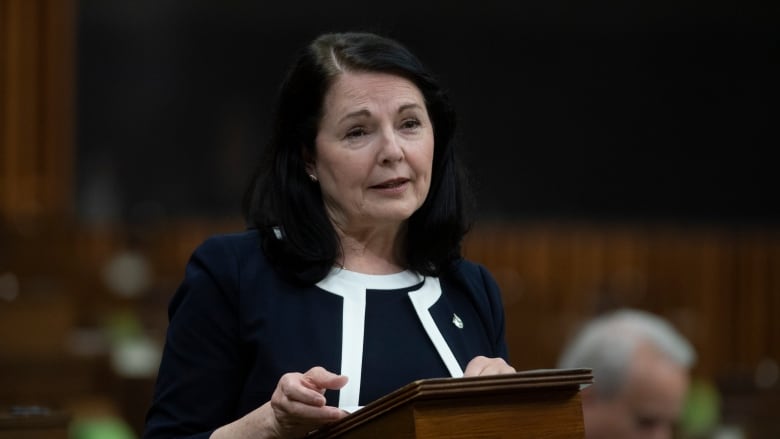 A woman wearing a dark blouse speaks at a podium in the House of Commons.