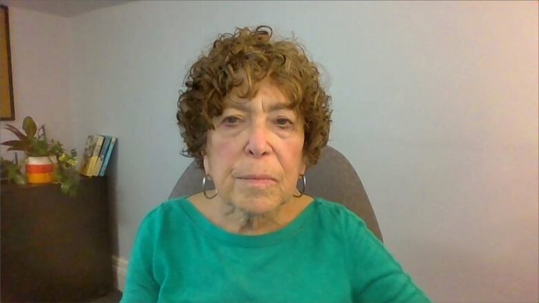 An older woman with shortly, curly brown hair wearing a green shirt.