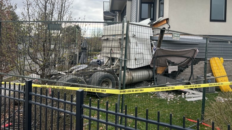 A truck being embedded into a house, with fencing around.