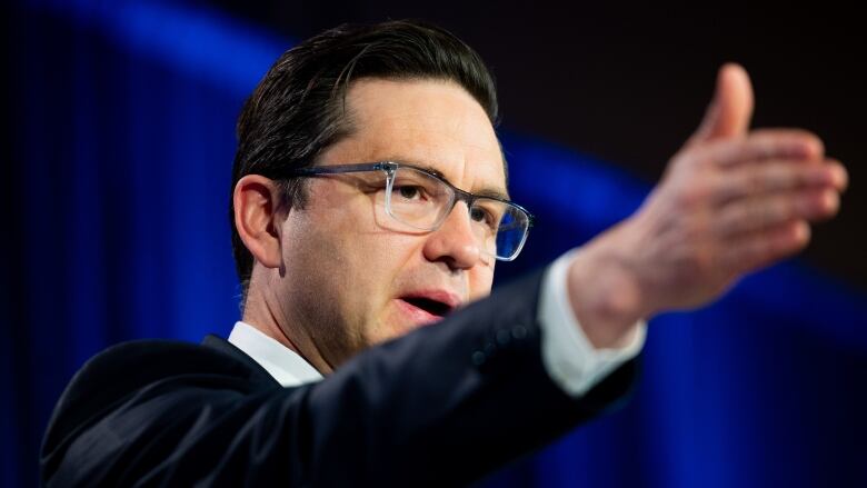 A politician gestures an arm forward while giving a speech.