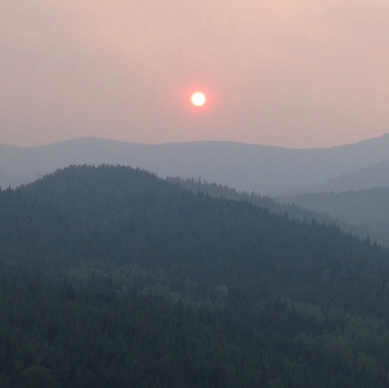 Hazy skies are seen around a dull sun over the mountains of British Columbia.