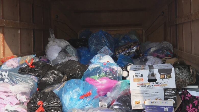 Piles of garbage bags filled with various items sit in a wood-pannelled trailer. An air fryer box is also in the trailer.