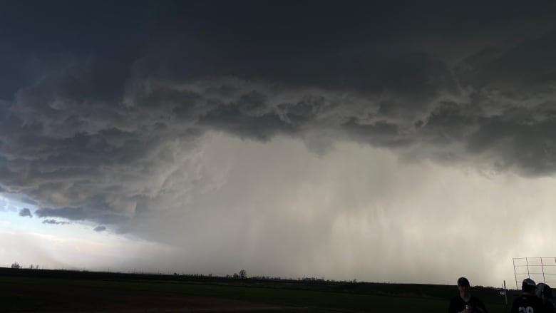 Dark clouds hang above a field. Heavy rain can be see in a distant blur.