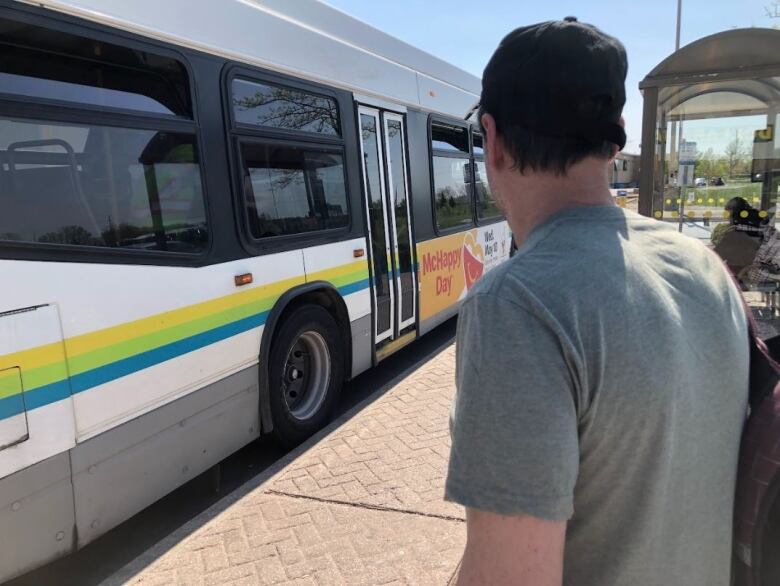 A man wearing a green t-shirt and a black hat about to board a bus