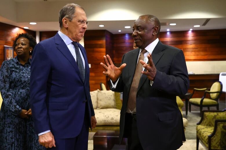 Two men in suits are seen in conversation inside a paneled room.