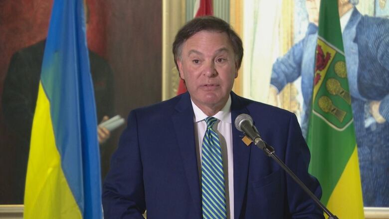 A man in a blue suit can be seen speaking at a podium. 