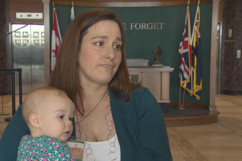 A woman in a green cardigan holds a baby.