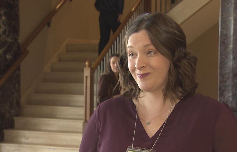 A woman in a purple sweater stands in front of a staircase.