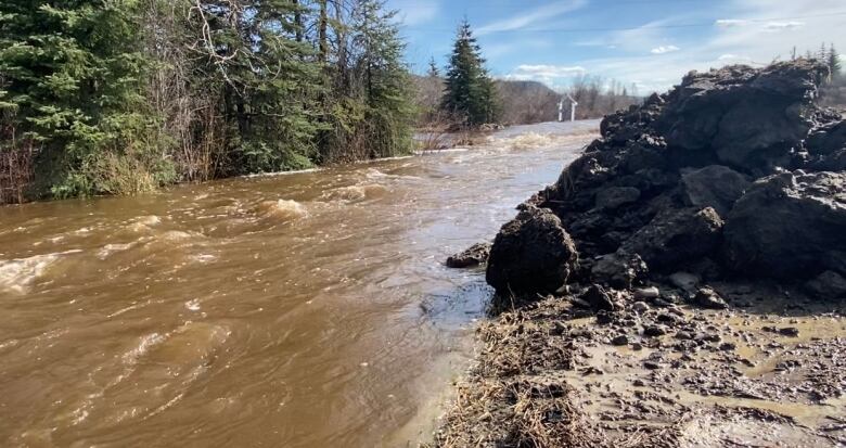 A rushing river is seen with rocks piled on the bank.