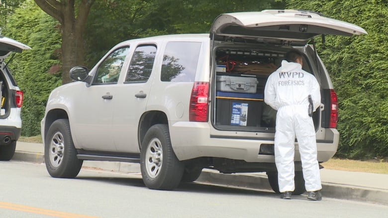 A man clad in a white forensic cover suit with WVPD forensics stencilled on the back works at the rear of a white van with its hatch open.