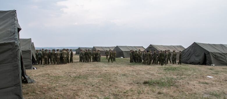 A row of army tents and dozens of soldiers in dark uniforms. 