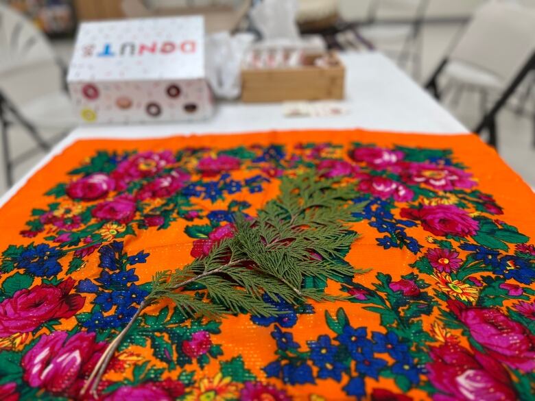 A cedar bough on orange and brightly coloured handkerchief, a box of donuts in the background. 