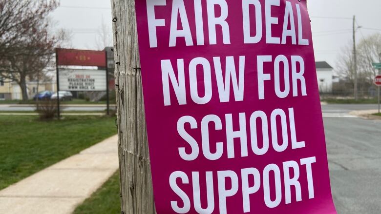 A pink poster stapled to a utility pole reads Fair Deal Now For School Support.