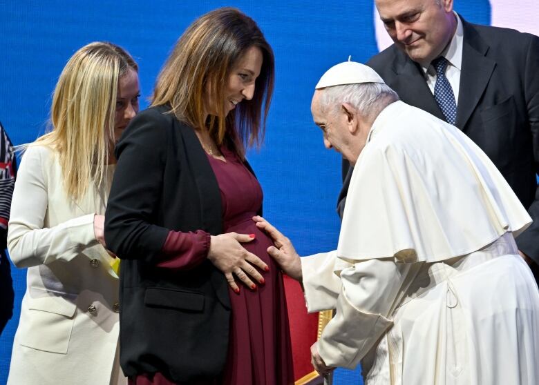 The pope touches a woman's pregnant stomach while two other people look on.