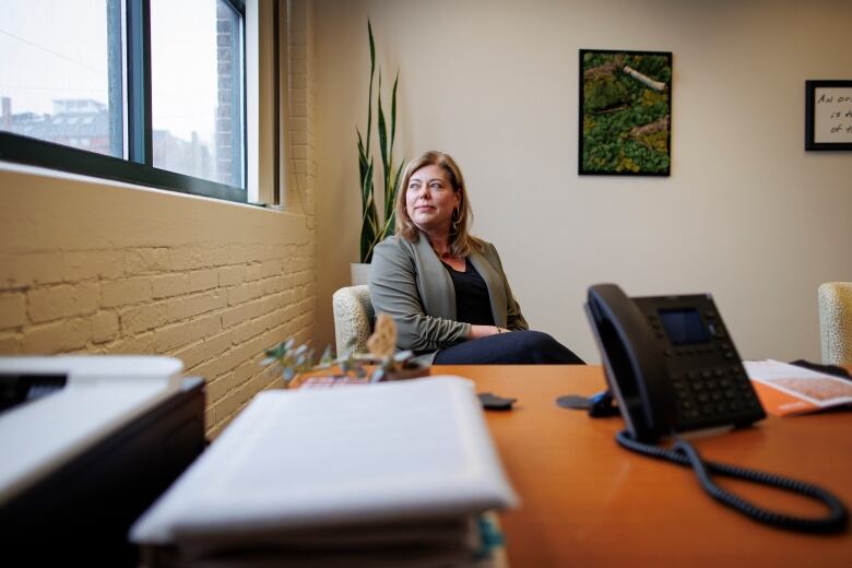 A woman sits in an office, looking out a window.