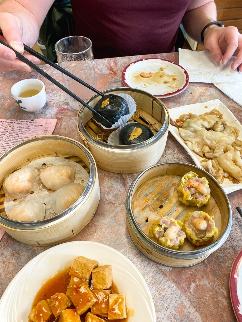 A selection of Chinese food sits in different plates and containers on a table top.