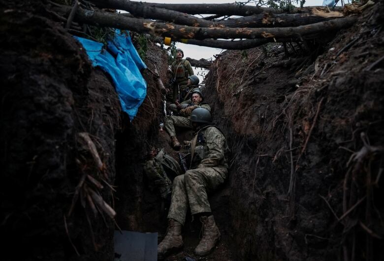 Soldiers are seen huddled inside a trench.