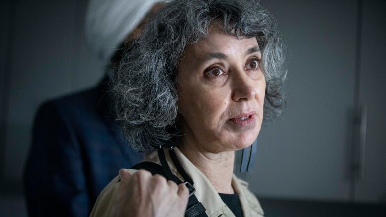 A woman with curly gray hair speaks to reporters in a darkened room.