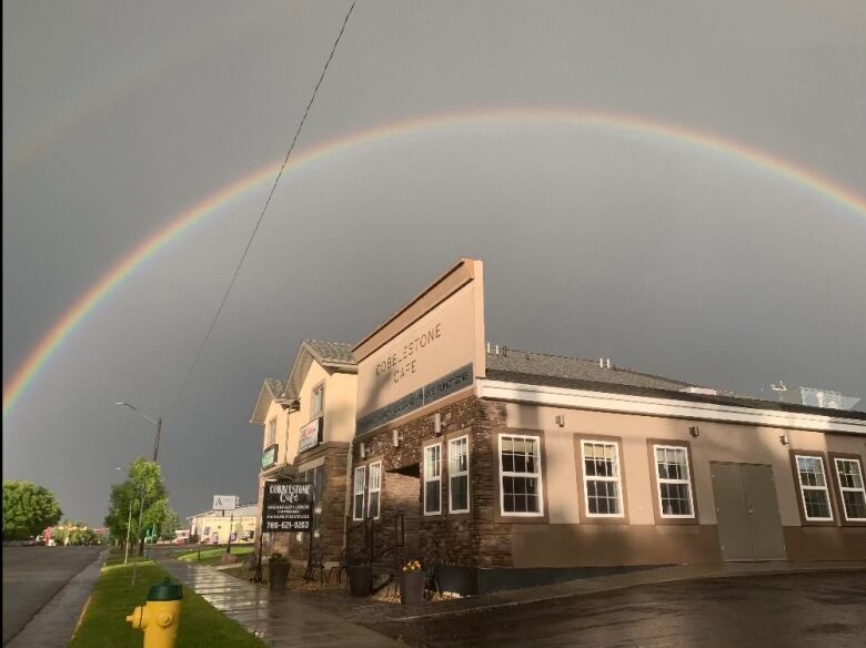 A cafe building is seen in front of grey skies and a rainbow.