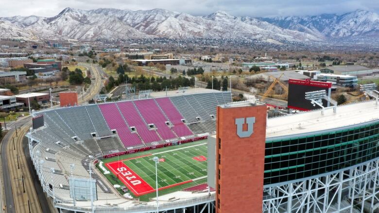 A huge football stadium stands in front of a small city with mountains in the background.