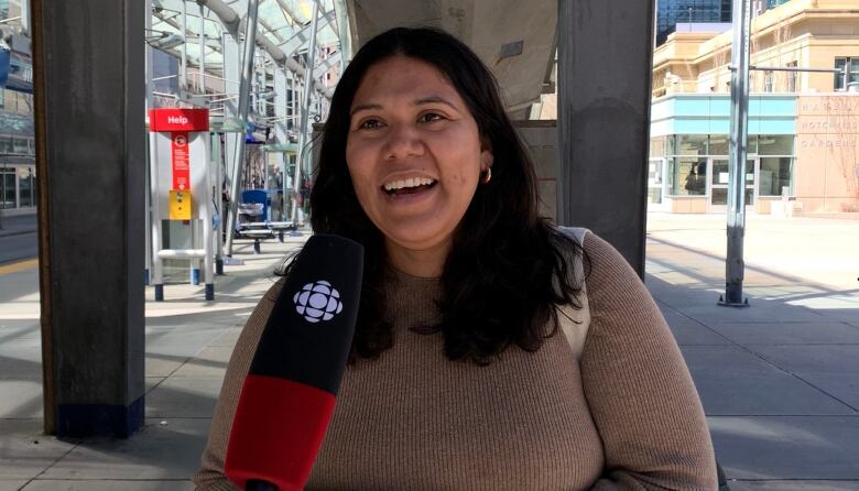 A woman speaks to a camera while standing near a set of CTrain tracks.