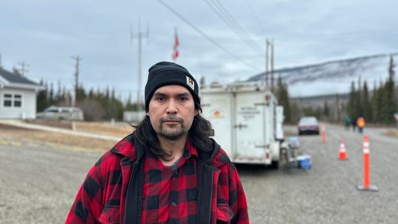 The photo shows a man looking directly at the camera, wearing a hunter shirt with a tuque. 