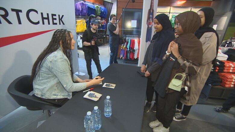 Girls meet a woman behind a table, who is signing an autograph.