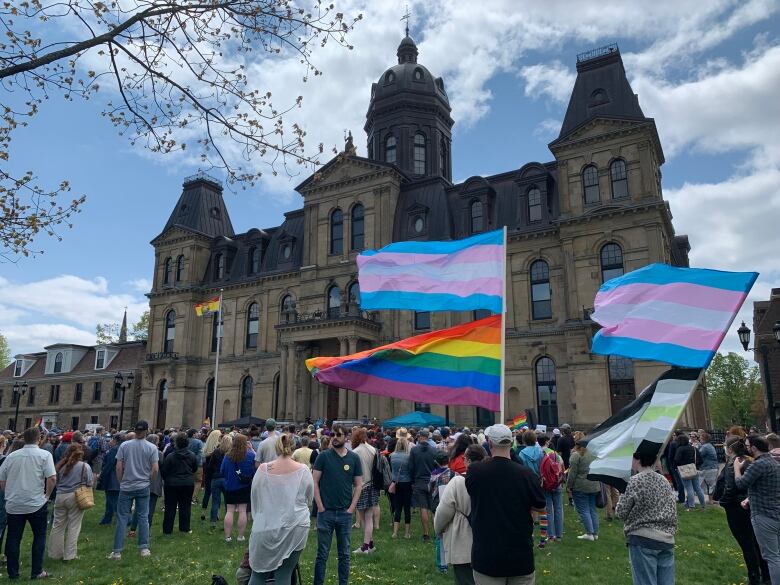 A group of people stand outside a historical building. Several people are carrying large pride flags.