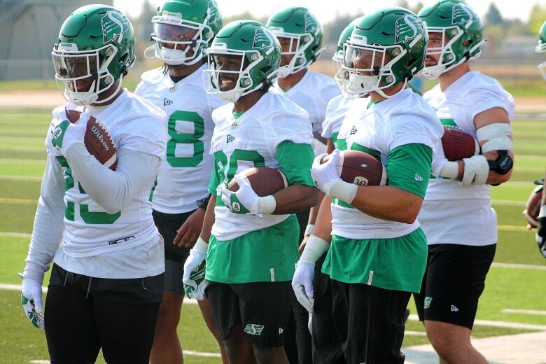 A group of seven players holding footballs stand together.