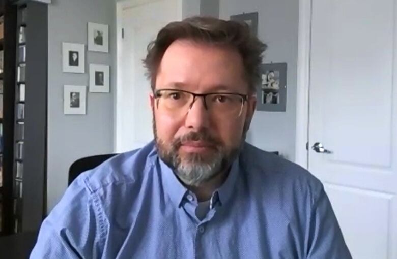 A man with brown hair wearing glasses and a blue shirt