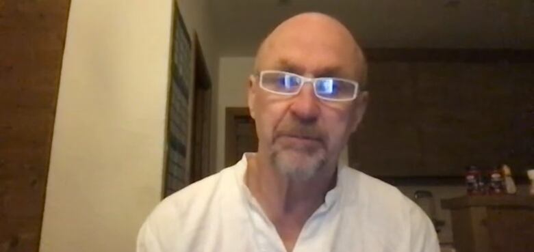 A bald man wearing a white shirt and glasses