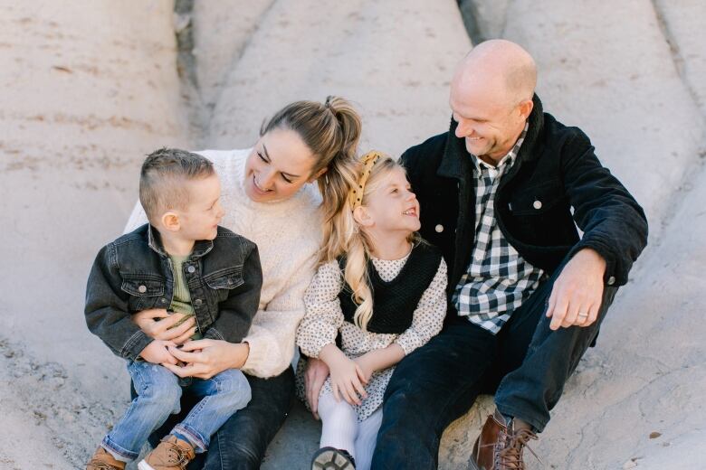 A man and woman sit outside with two children. They are all looking at each other and smiling. 