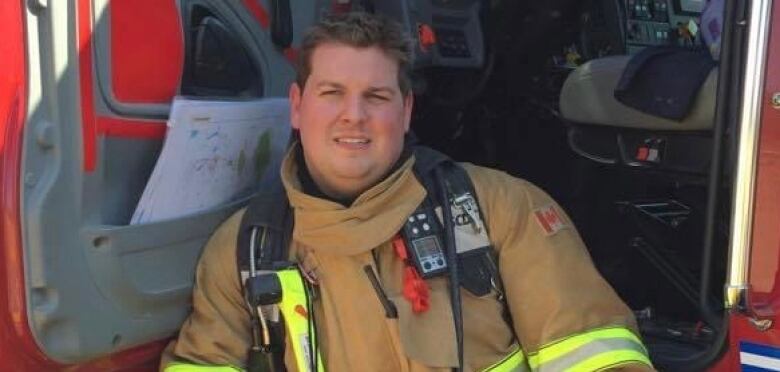 A man in a firefighter's uniform sits on the step of a fire engine.