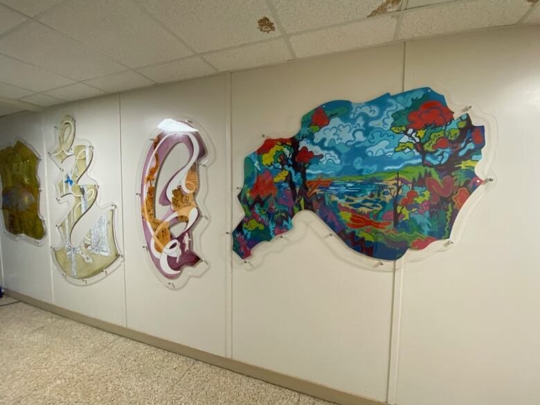 Four large pieces of artwork on display on a white wall, in a hallway.