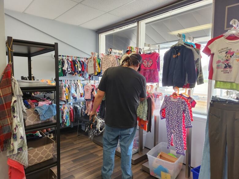 A man dressed in a black shirt looks through clothes in a shop while collecting hangers.