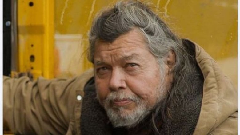 A man with grey hair, a beard and a parka looks at the camera with an intense gaze. 