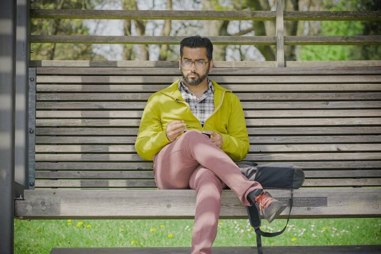 An Indian man sits drawing on a bench outside.