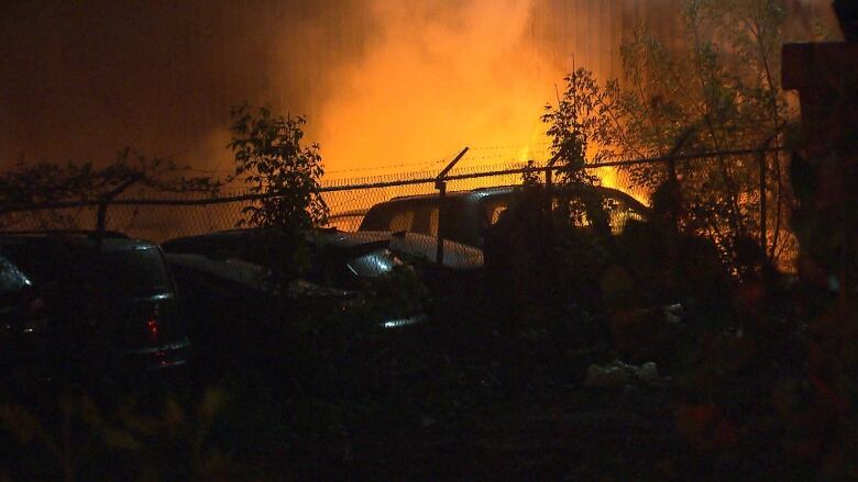 A dark photo of a fire burning close to vehicles. 