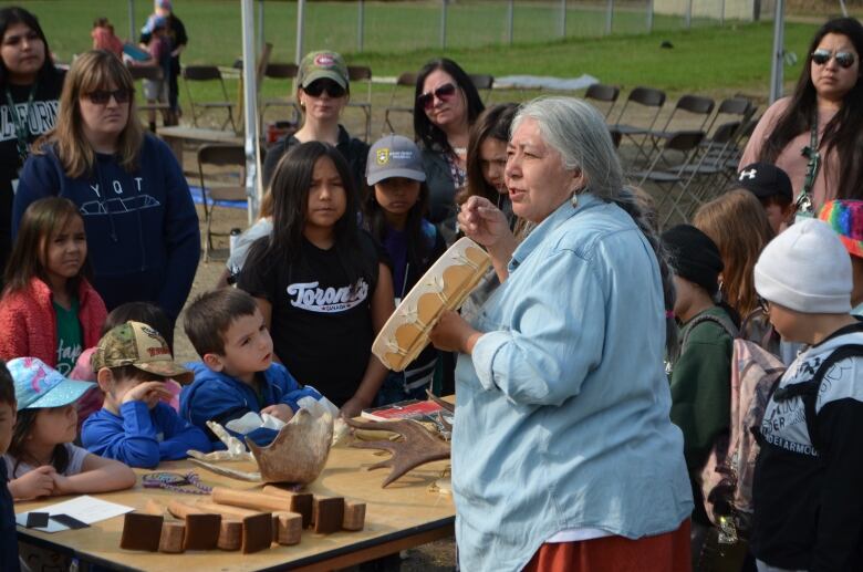 Children gather around an Indigenous teacher holding a hand drum. 