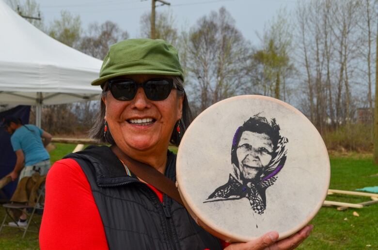 Woman in a hat holding hand drum while she is smiling 