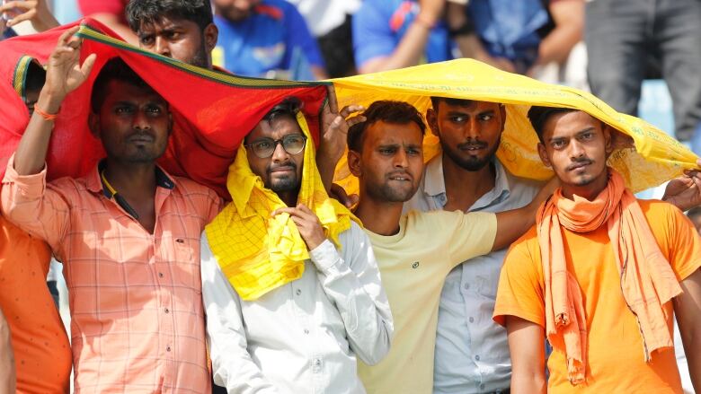 Four men shade themselves with a red and yellow flag.