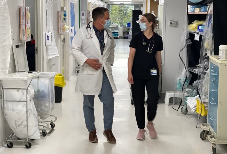 Two people in medical clothing walk down a hospital hallway.