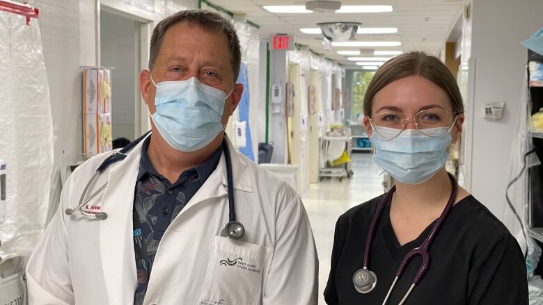 A man in a while coat and a woman in dark scrubs wearing glasses.