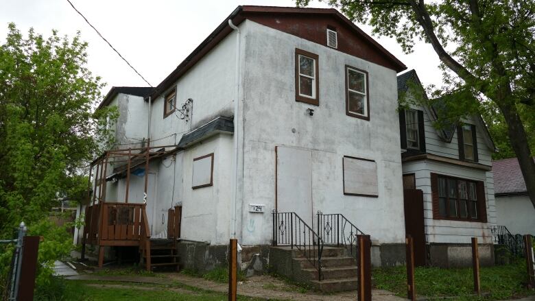 A white two-storey house with boarded up windows. 